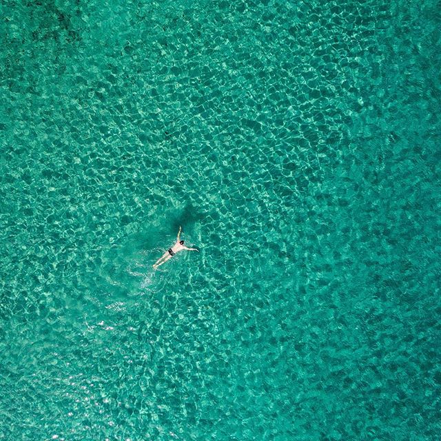 Aerial view of a single person swimming in crystal-clear turquoise water, creating a sense of peace and escape.