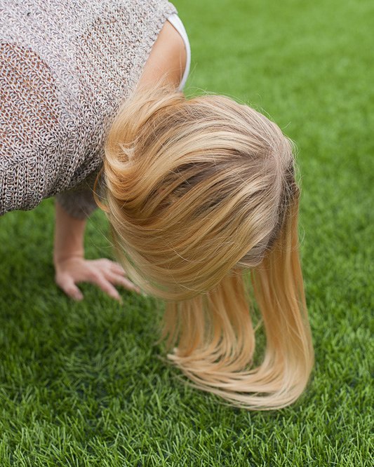 Woman with blonde hair bending over on green grass. Focus on healthy lifestyle and mindfulness.
