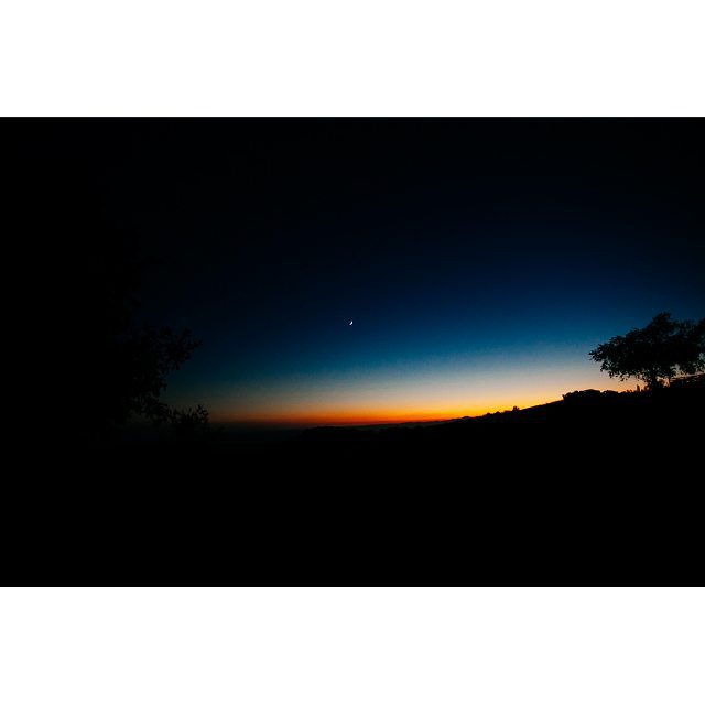 The tranquil night sky features a crescent moon illuminating the dark landscape at twilight.