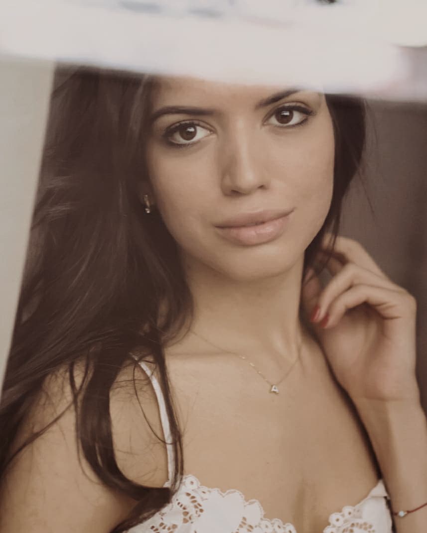 Portrait of a serene brunette woman with a delicate necklace, posing indoors in soft light.