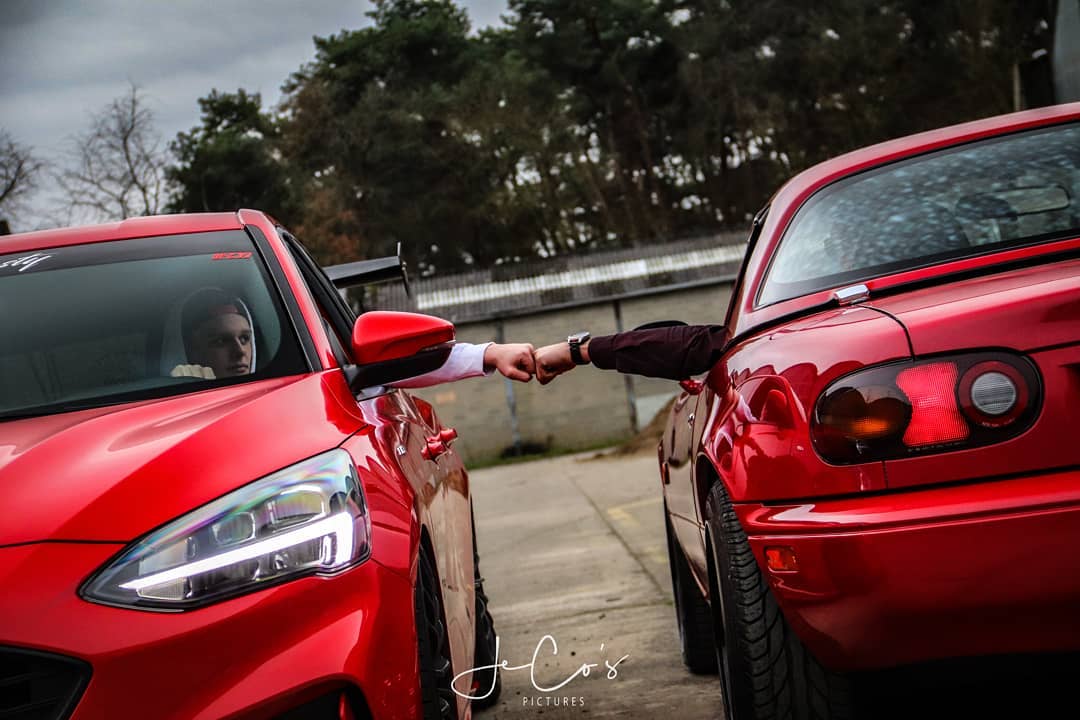 Two red cars are fist bumping on a road.