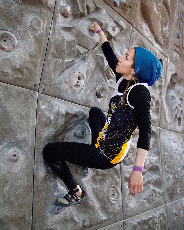 A woman rock climbing on an indoor wall demonstrating strength and determination.