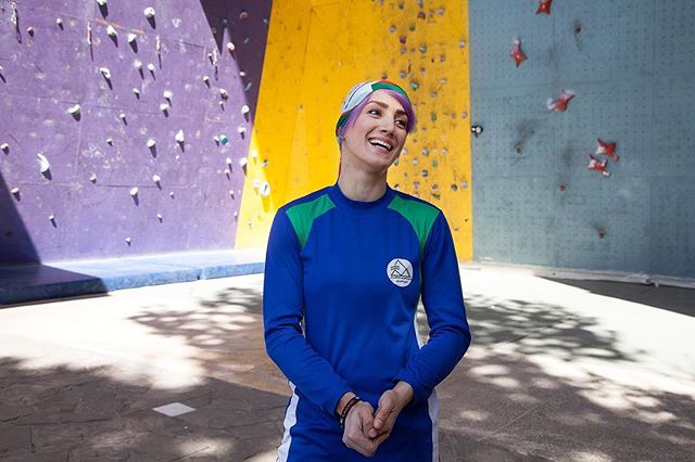 A smiling female climber stands in front of a climbing wall, promoting fitness and a healthy lifestyle.