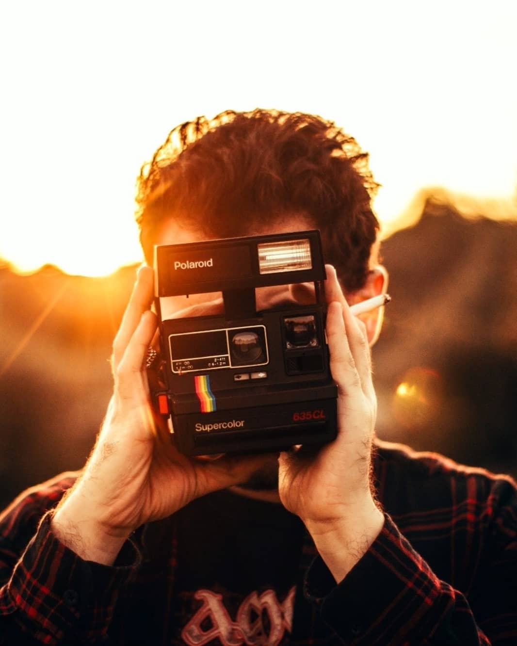 A man holds a vintage Polaroid camera, capturing a moment with a retro flair in warm light.