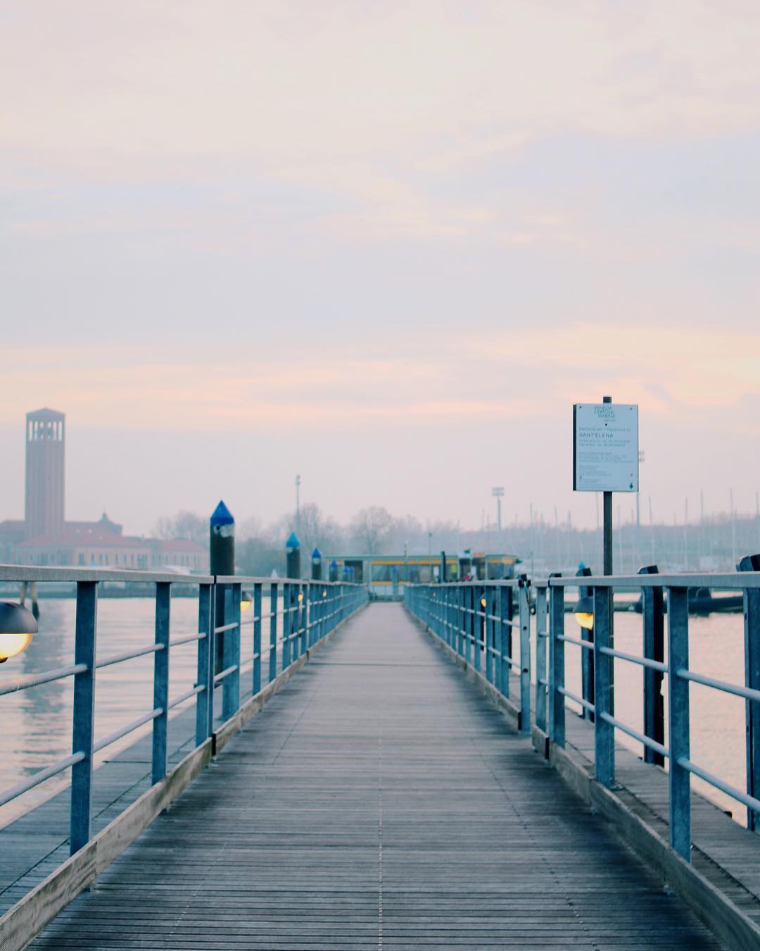 A tranquil view of a wooden pier extending into the calm waters of Venice, Italy under a soft sky.