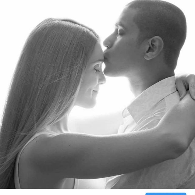 A couple shares an intimate moment as the man kisses the woman's forehead in this black and white portrait.