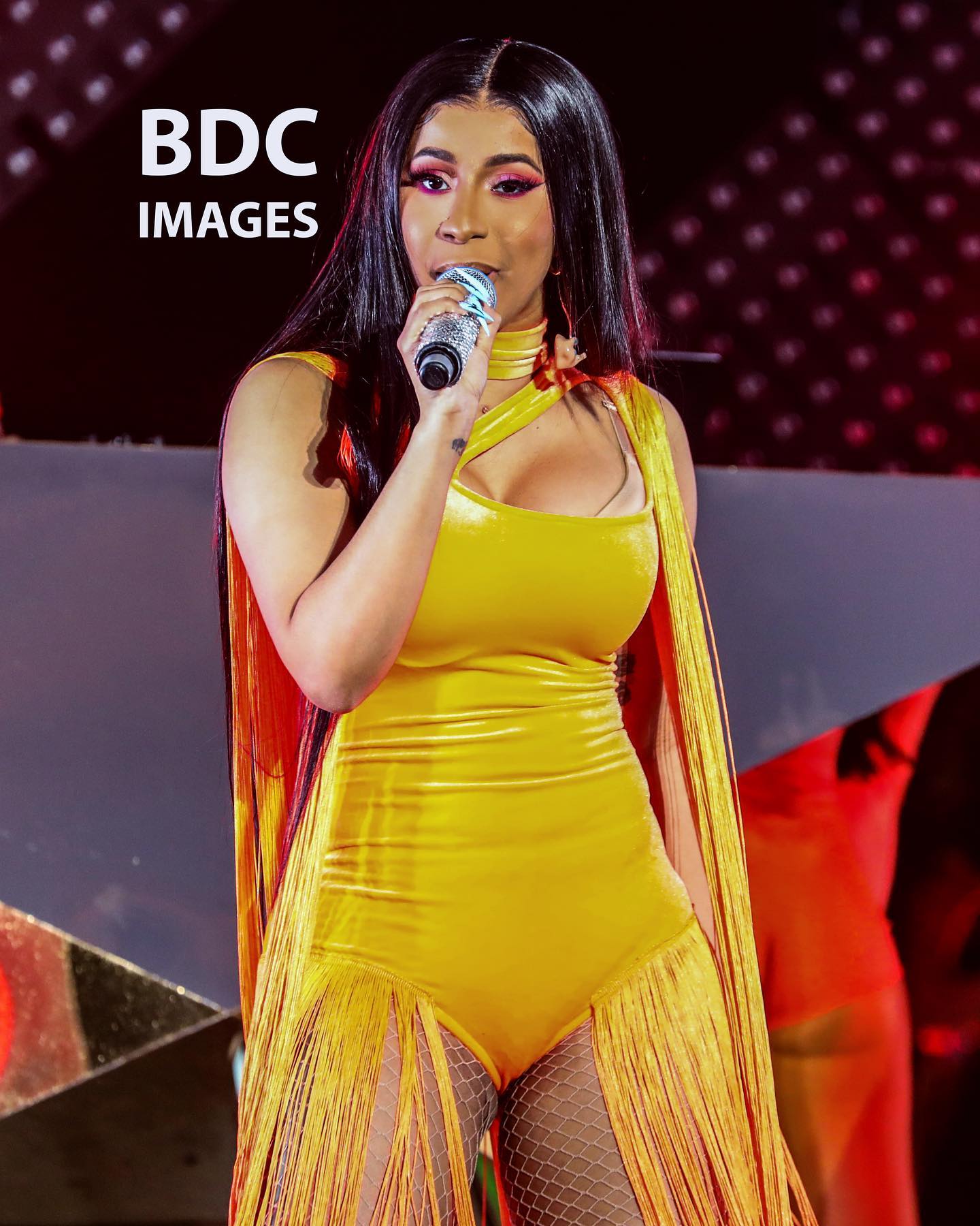 Cardi B performs on stage in a vibrant yellow outfit. Confident and energetic performance.