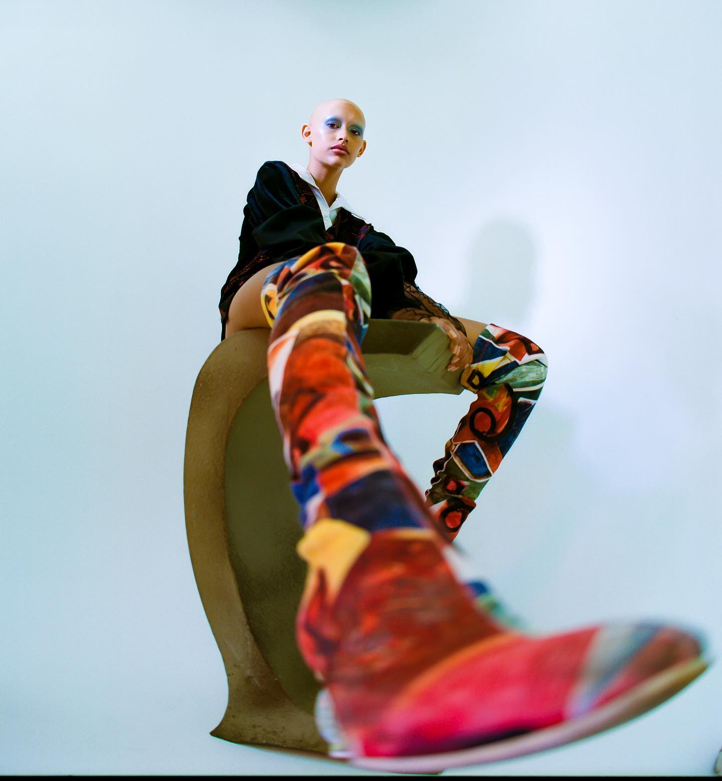 A bald woman in patterned boots poses in a studio with a low angle shot emphasizing fashion.