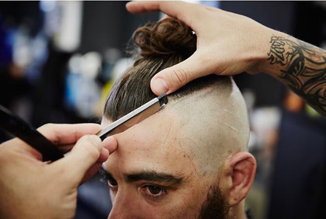 A barber shaves a man's head with a straight razor in a close-up, modern barbershop setting.