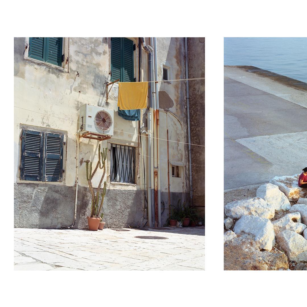 A quiet mediterranean street scene with old buildings, yellow towel hanging, and a cactus in a pot.