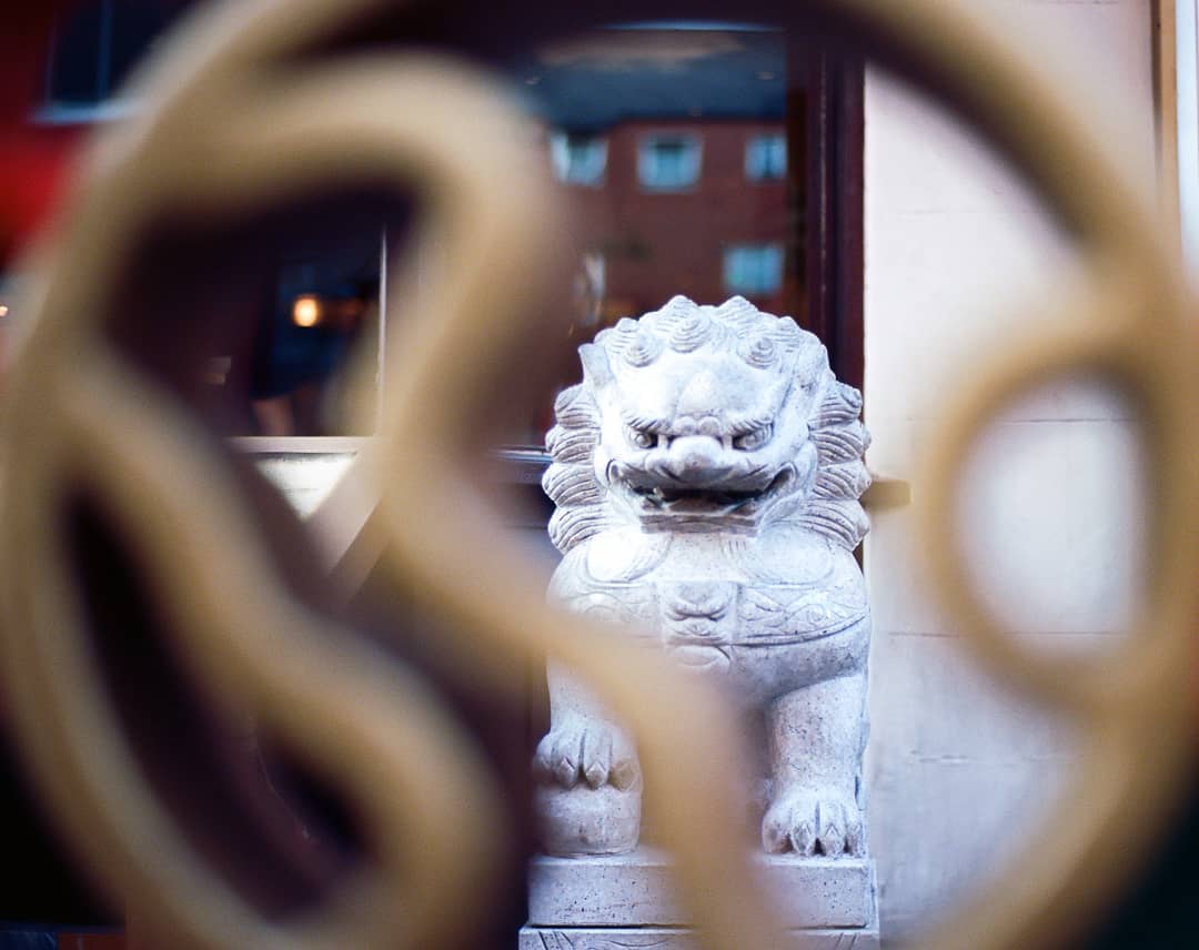 A stone Chinese guardian lion statue stands guard, blurred by ornate metalwork in the foreground.