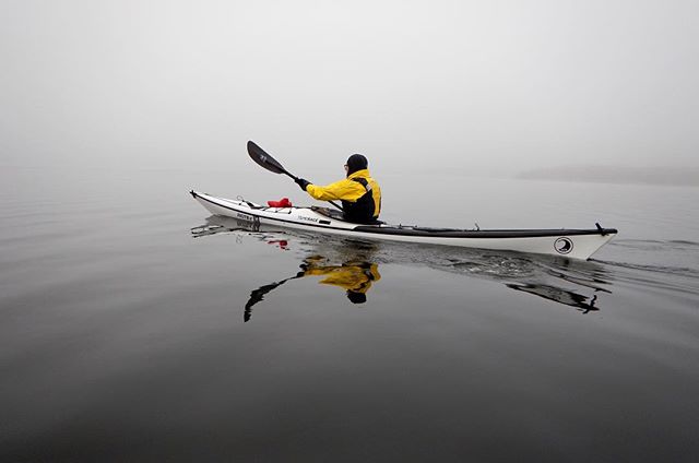 A man in a yellow jacket kayaks on a foggy lake, enjoying a peaceful day of paddling.