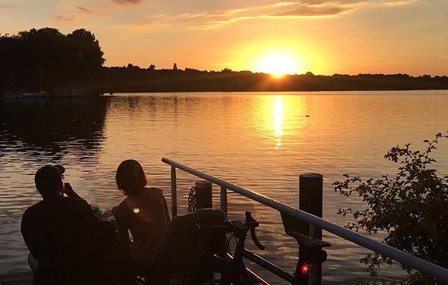 A couple enjoys a serene sunset by the lake on a pier with their bicycle, creating a peaceful outdoor scene.