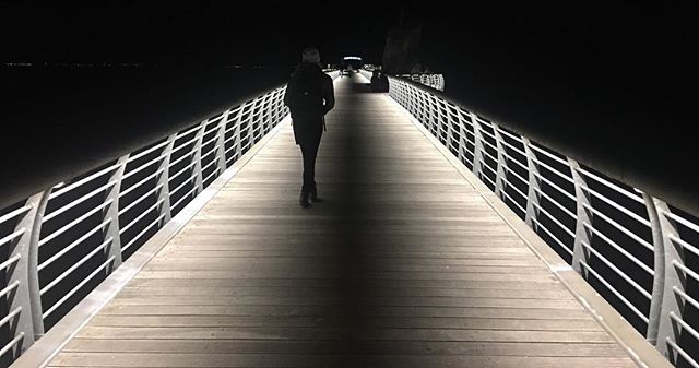 A person walks alone on a brightly lit pier at night.