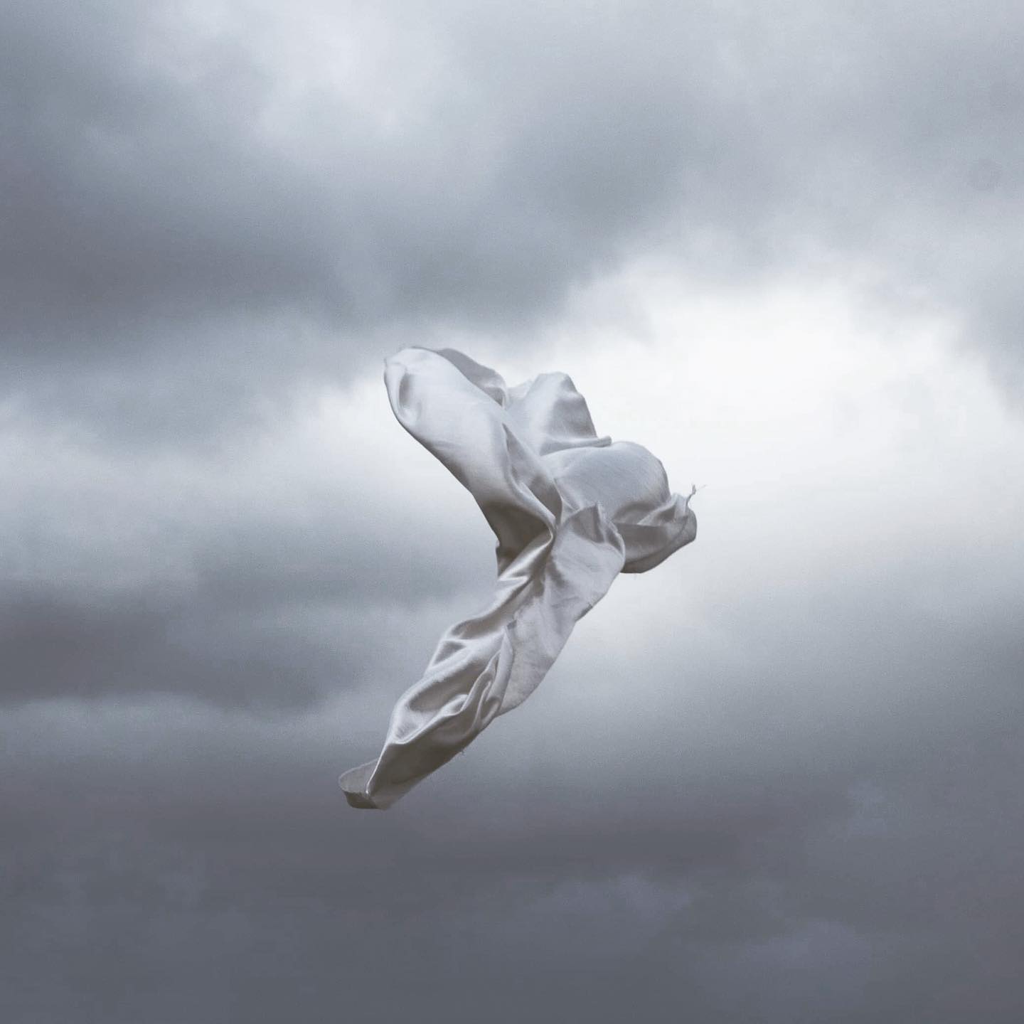 A piece of white silk floats gracefully in a cloudy sky, creating a tranquil and ethereal scene.