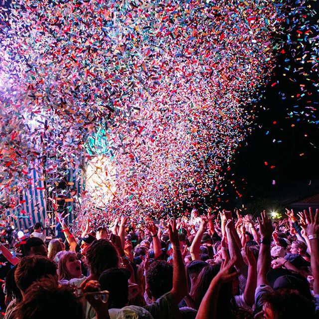 A large crowd celebrates under a shower of colorful confetti at an exciting outdoor event.