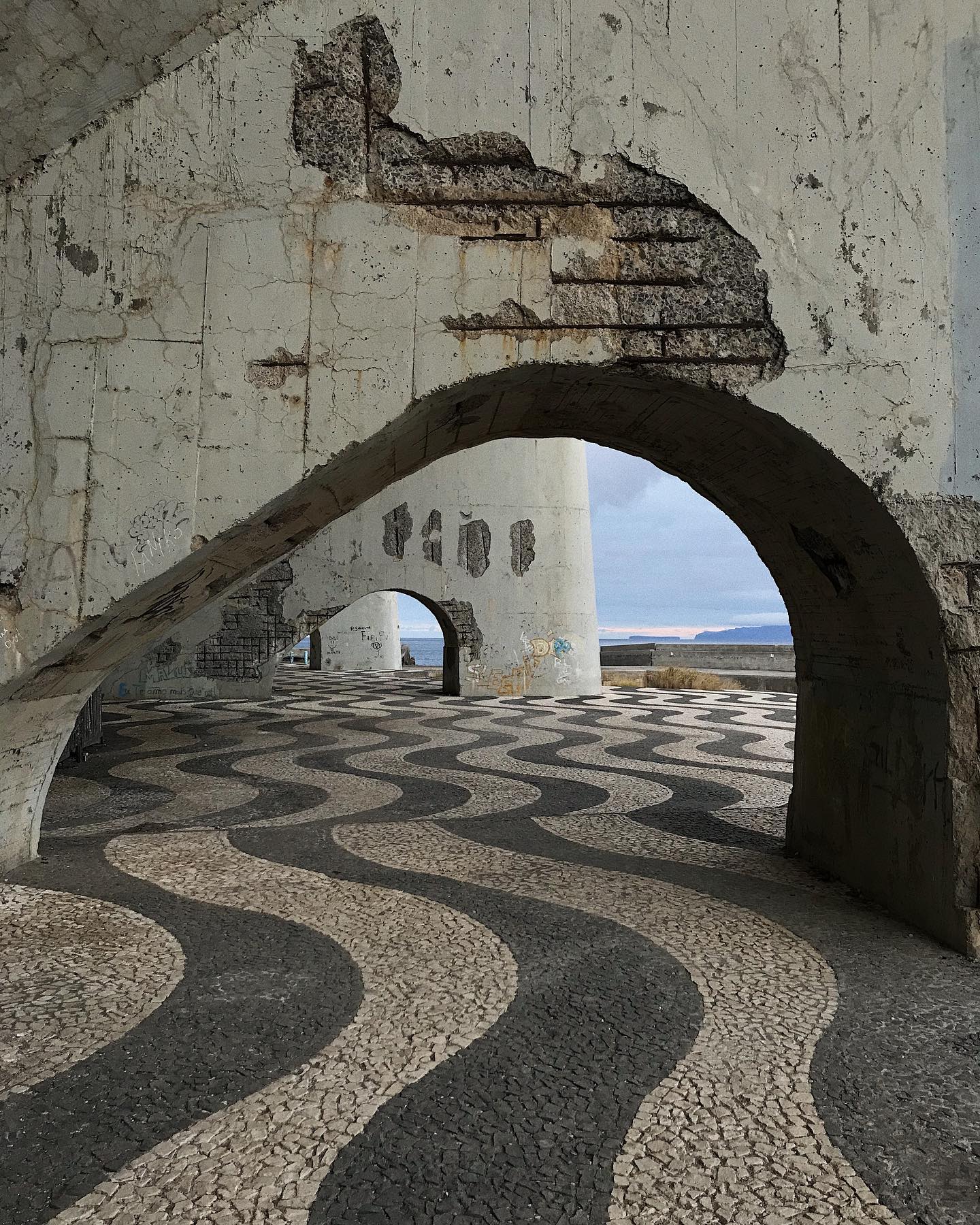 Coastal architecture featuring stone arches and a patterned walkway creating a tranquil urban scene.