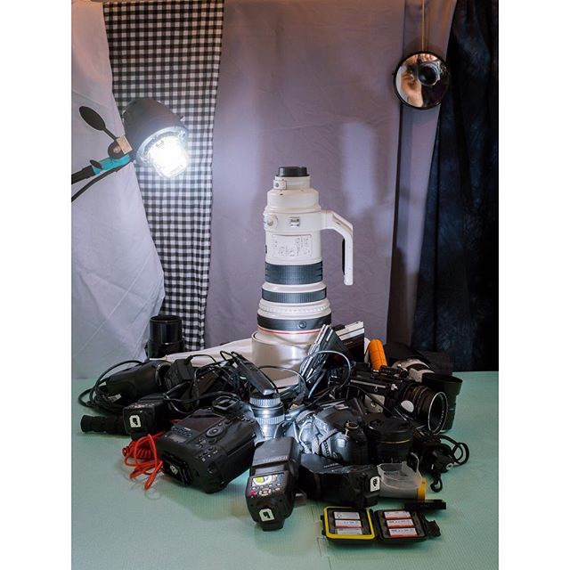 A collection of cameras and photography equipment, including a large lens and flashes, sit ready for use.