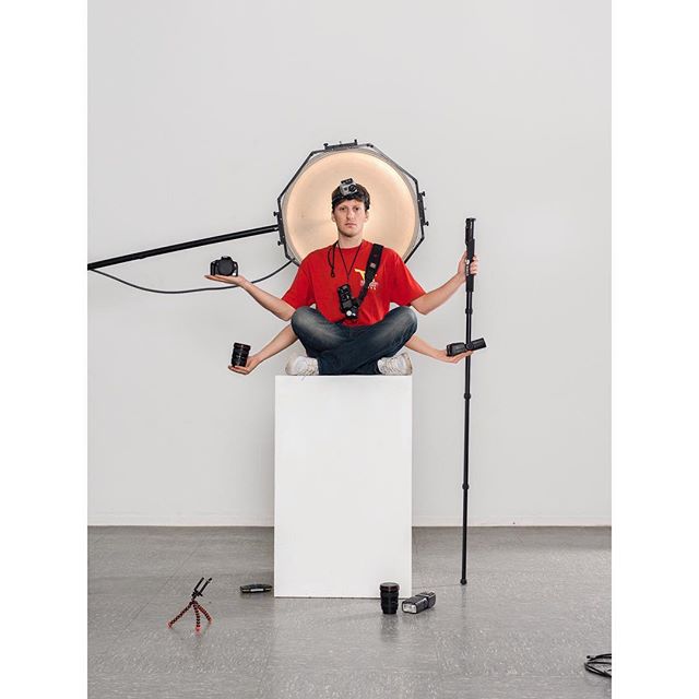 Man with multiple arms sits on a box surrounded by photography equipment in a studio.