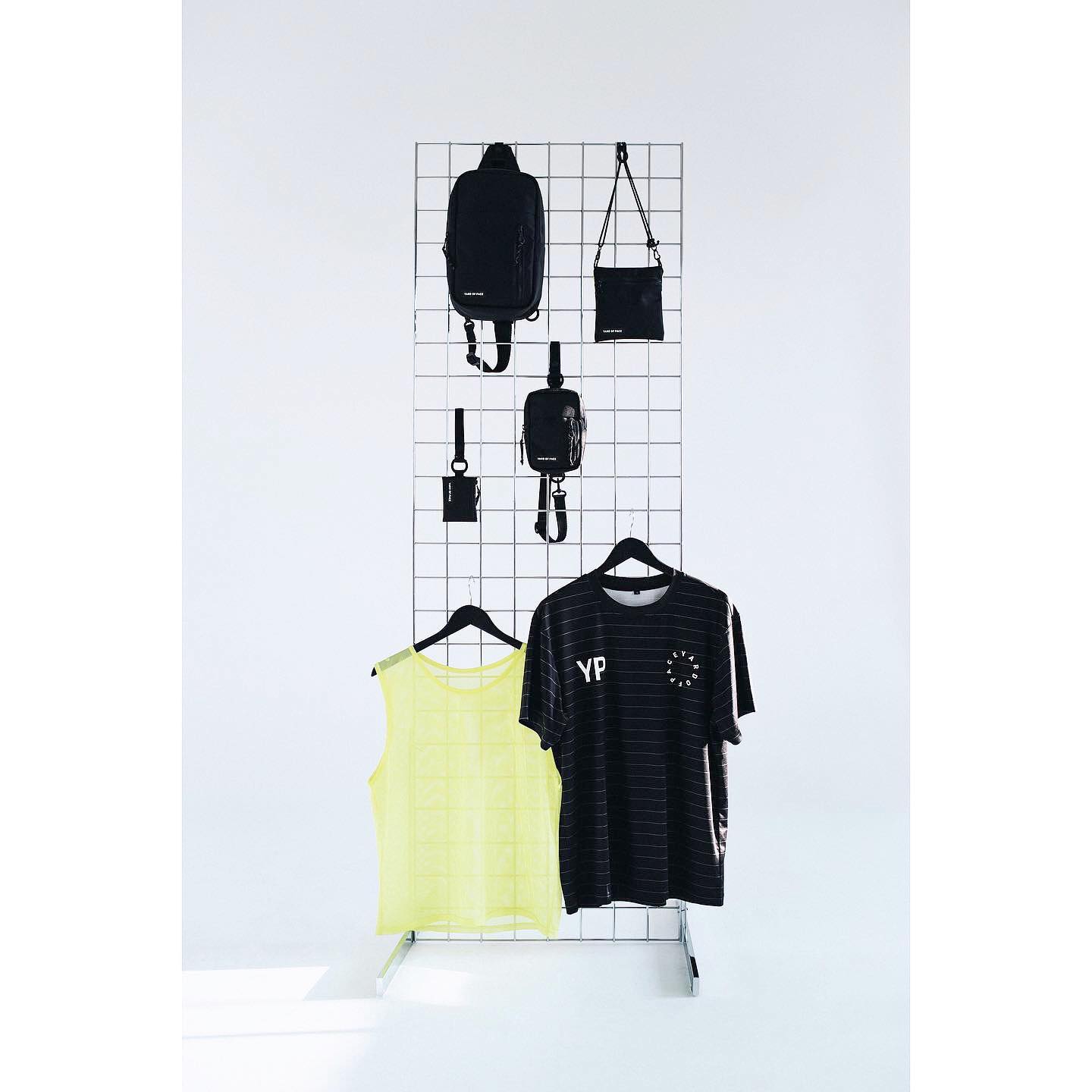 Clothing and accessories on a white grid, featuring t-shirts, bags and fashion items in a minimalist studio setting.