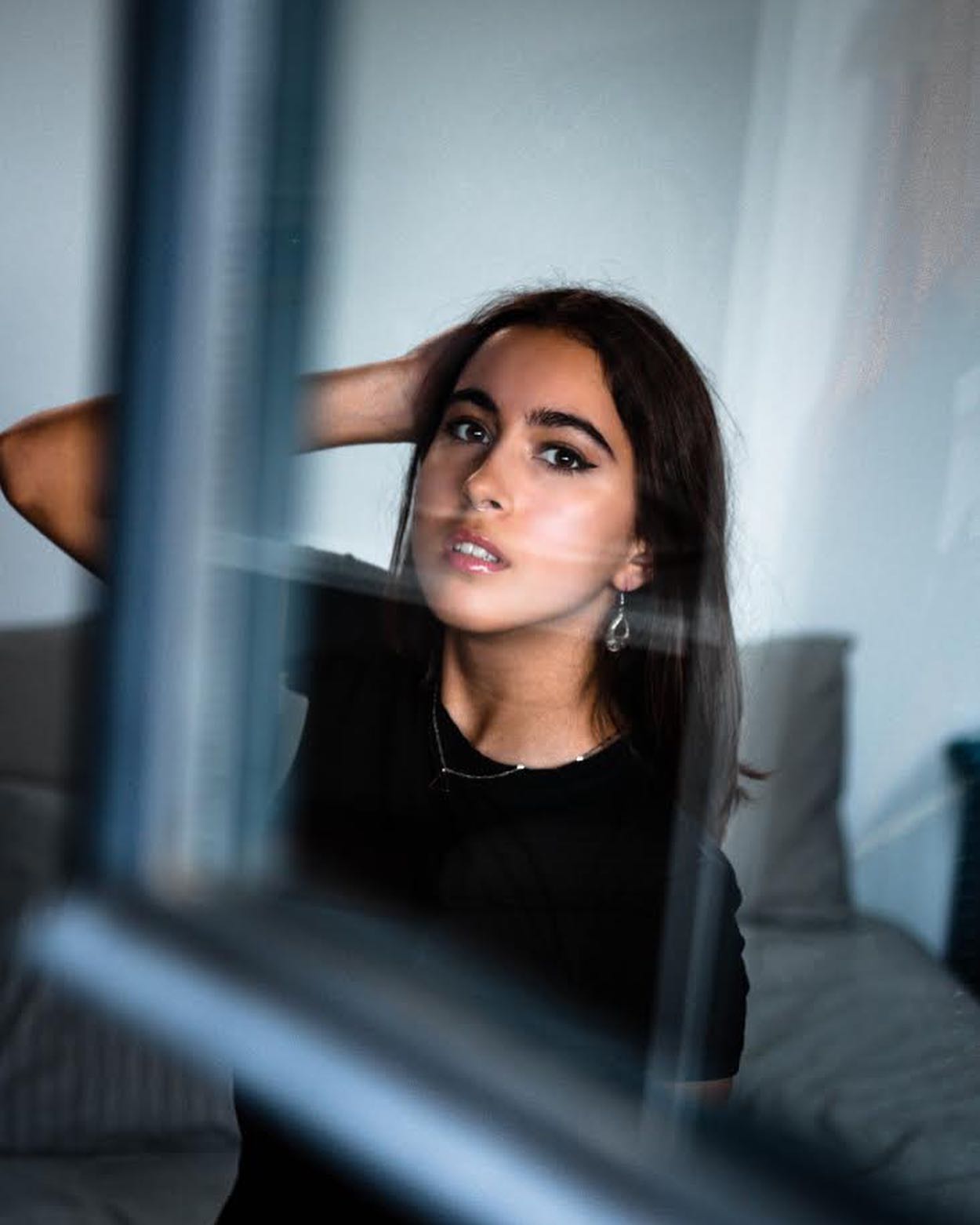 A young woman poses gracefully with her hand on her head in a natural indoor setting.