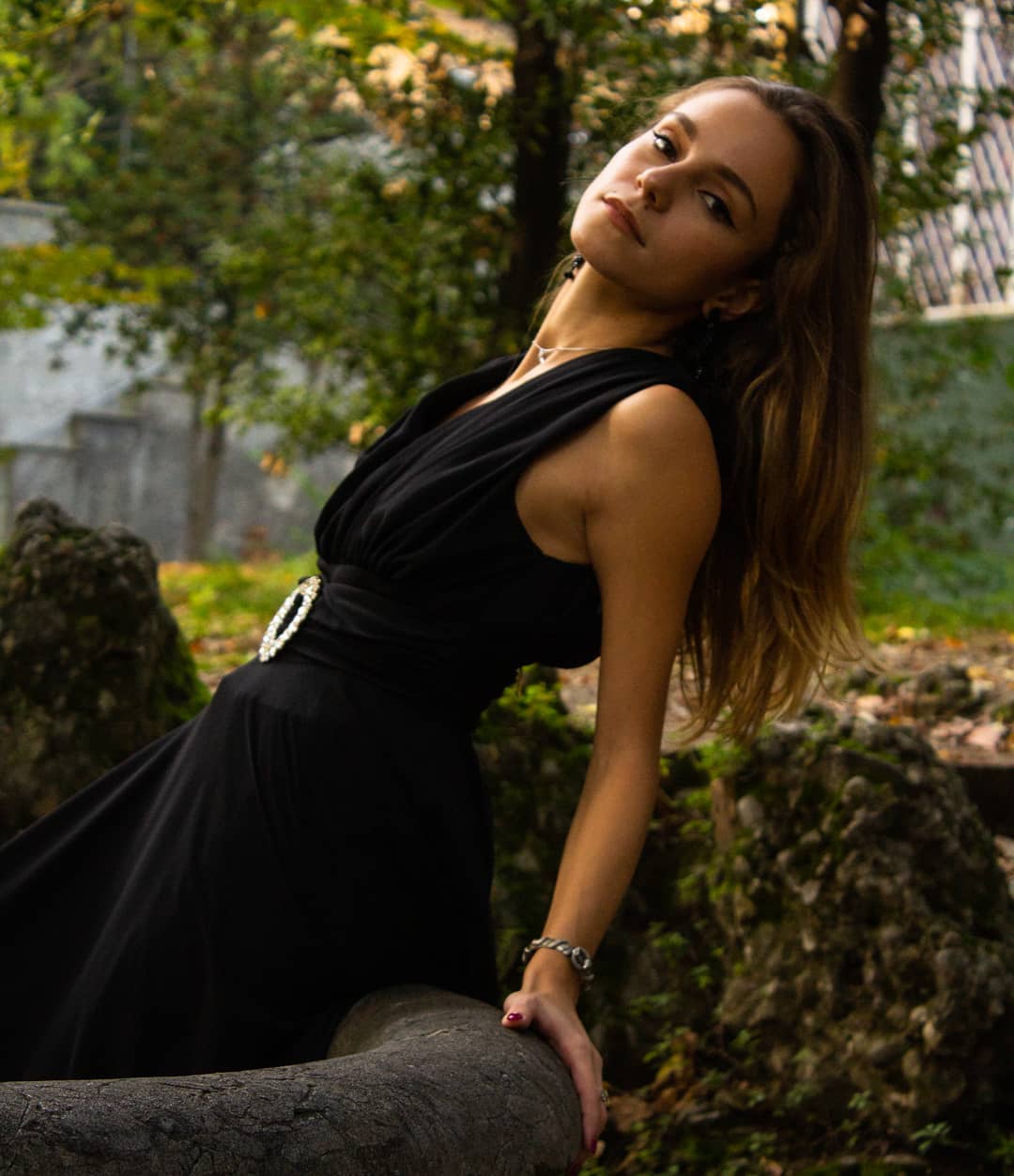 A woman in a black dress poses elegantly in a garden, showcasing a blend of confidence and serenity.