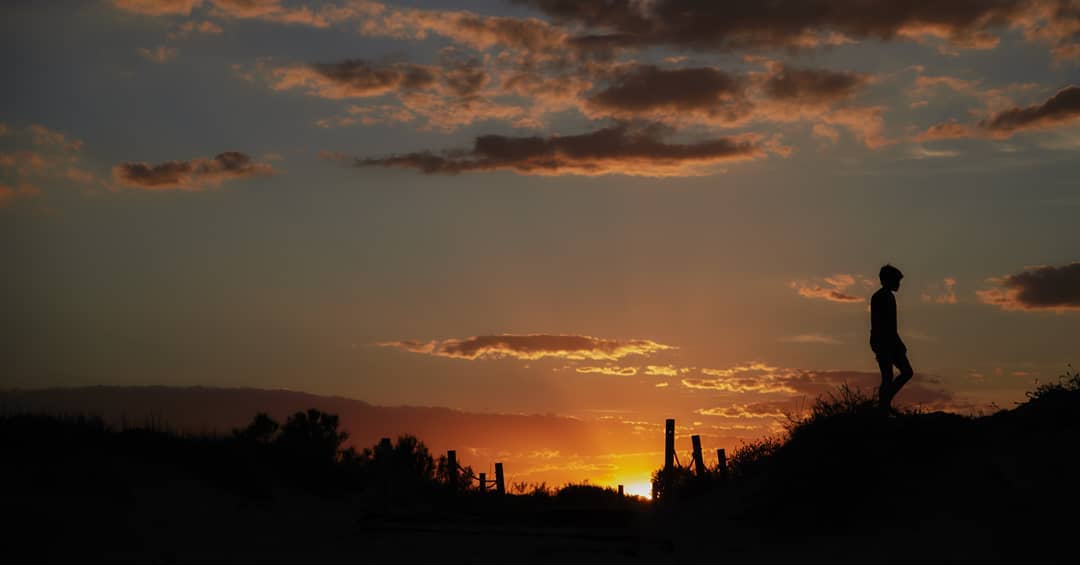 A silhouetted figure stands against a vibrant sunset, creating a tranquil scene of nature and contemplation.
