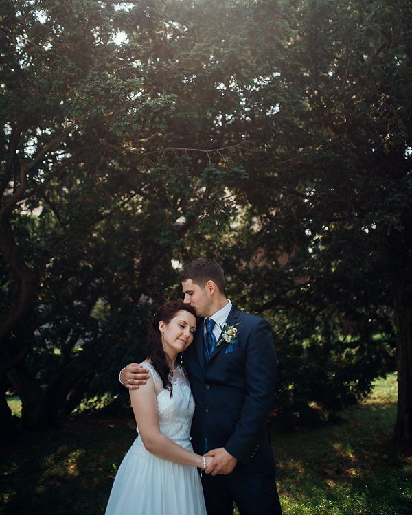 A bride and groom embrace under a tree in a wedding photo filled with romance and warmth.
