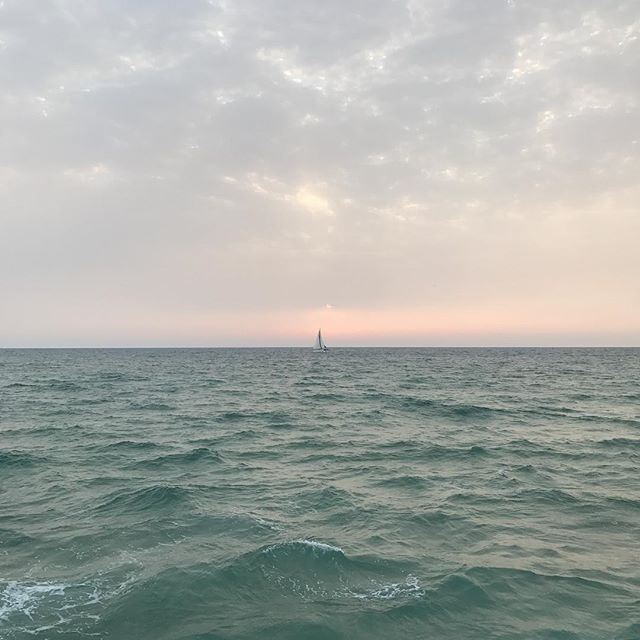 A lone sailboat glides on the ocean under a soft, pastel sky at sunset, creating a serene and tranquil seascape.