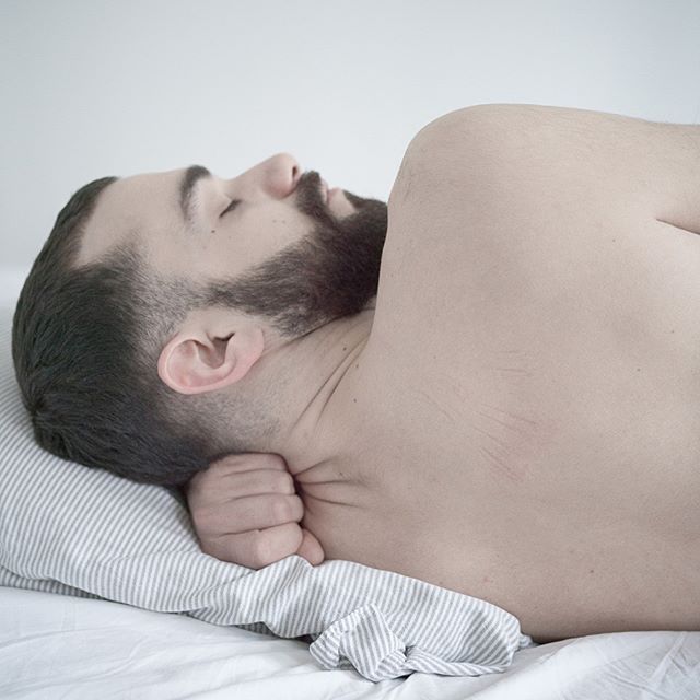 A bearded man peacefully sleeps on a striped pillow in a serene and calm bedroom setting.