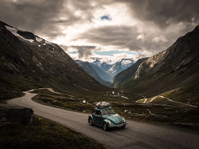A classic Volkswagen Beetle drives on a winding road through a scenic mountain valley, ready for adventure.