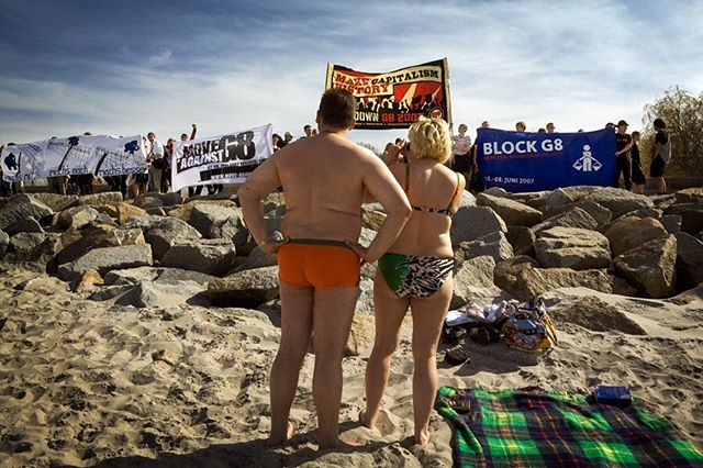 People protest with banners at a beach gathering, standing against capitalism during the G8 summit.