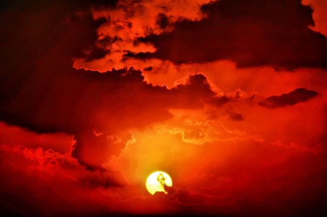A fiery sunset with a silhouetted figure against dramatic red clouds, evokes a sense of power and mystery.