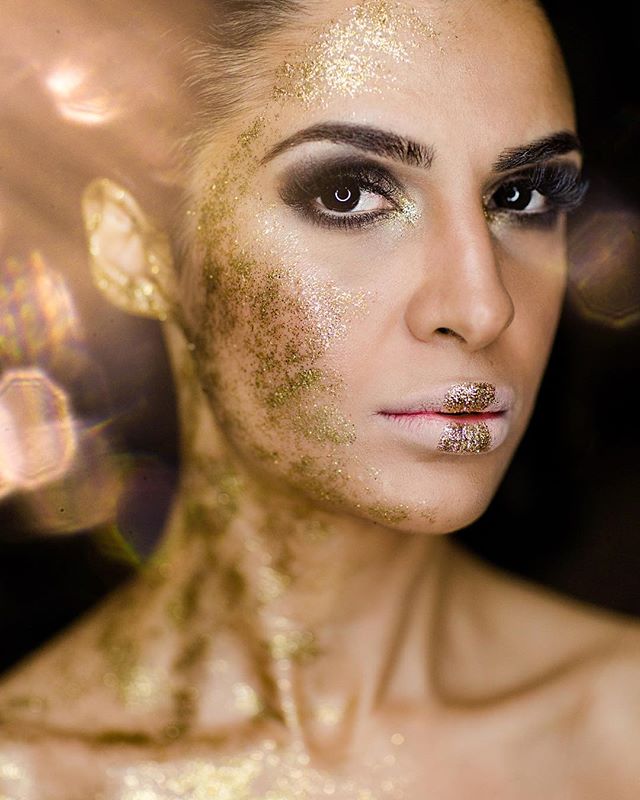 A woman with gold glitter makeup poses in a close-up shot for a beauty editorial.