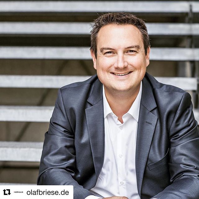 Professional businessman in suit smiles confidently, sitting on stairs for a corporate headshot.