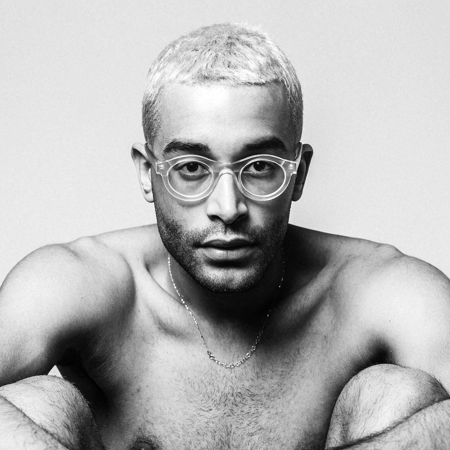 Striking black and white portrait of a confident man with glasses and a necklace.