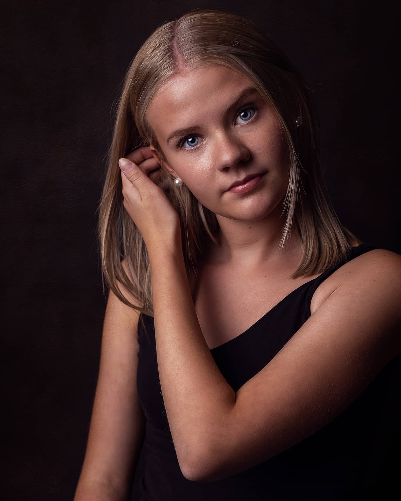 A serene young woman poses in a studio portrait, showcasing her youthful skin and soft features against a dark background.