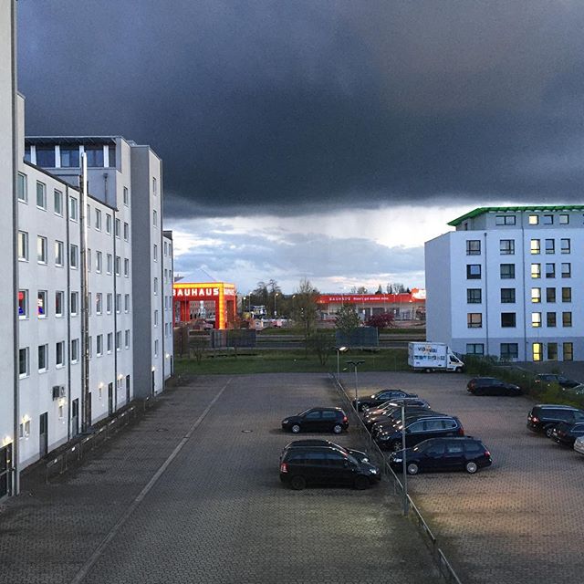 View of buildings and cars in a parking lot with a dramatic sky overhead in an urban setting.