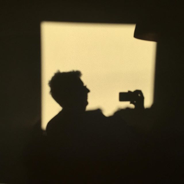 A silhouette of a man holding a camera is cast on a light yellow wall.
