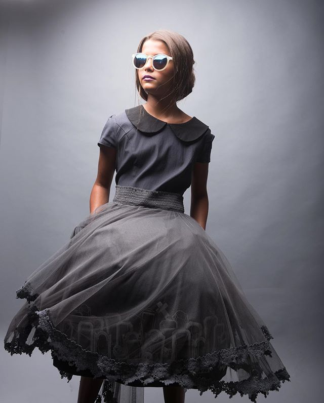 A stylish girl in a gray dress and sunglasses poses in a studio setting with soft lighting.
