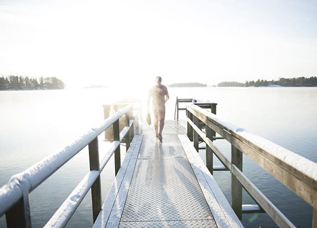 A man walks on a snow-covered pier toward a calm, serene lake on a bright winter day.