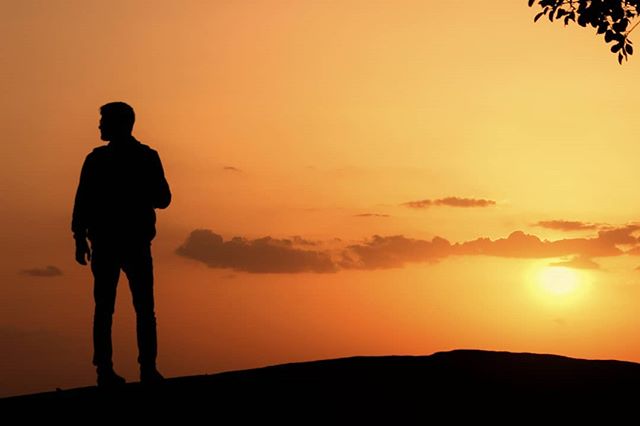 A silhouetted man looks out at a vibrant orange sunset from a hilltop, inspiring feelings of hope and motivation.