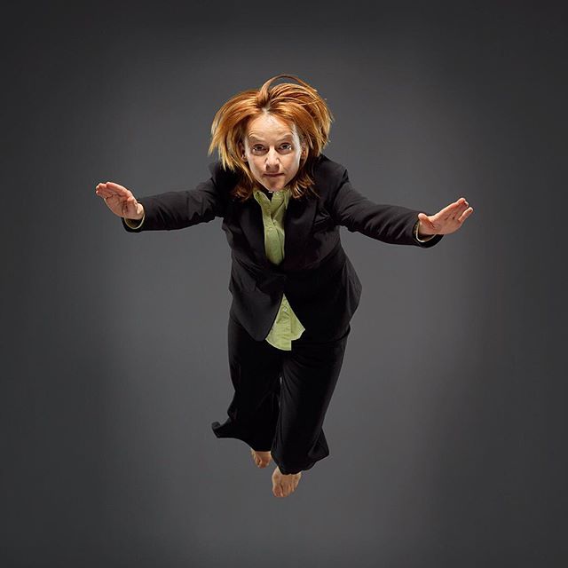 A businesswoman in a suit leaps in the air, exuding energy and confidence against a gray backdrop.