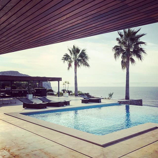 An infinity pool overlooks the ocean, lined with palm trees and sun loungers for a luxurious and relaxing getaway.