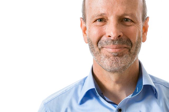 A cheerful middle-aged man with a beard smiles in a professional portrait against a white background.