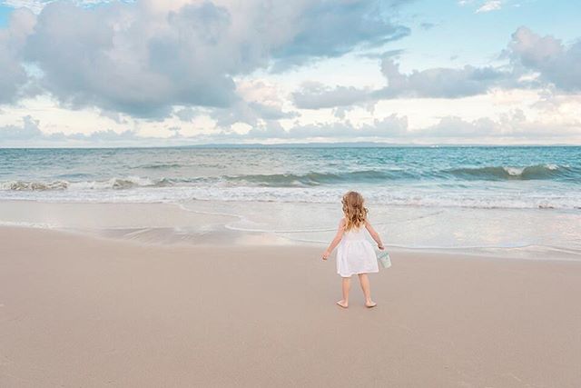 A young girl in a white dress walks towards the ocean on a tranquil beach.
