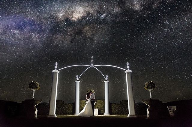 A bride and groom embrace under a starry sky on their wedding night. Romantic garden scene.
