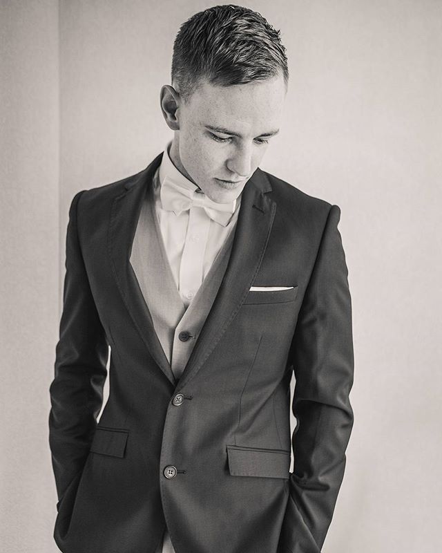 Monochrome portrait of a man in a classic tuxedo, looking down, for formal wear or event promotion.