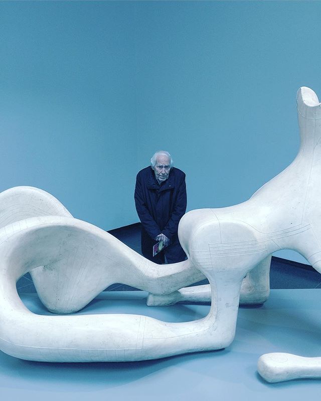 A man looks at a modern white sculpture in an art gallery against a blue wall.