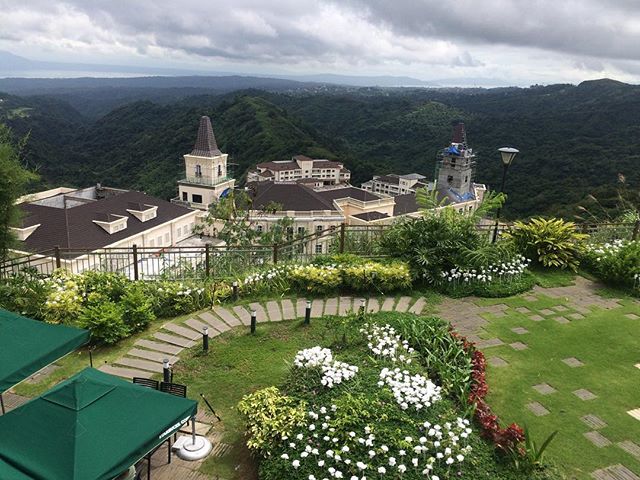 A scenic view of a building complex nestled in a mountainous landscape with lush greenery and walking path.